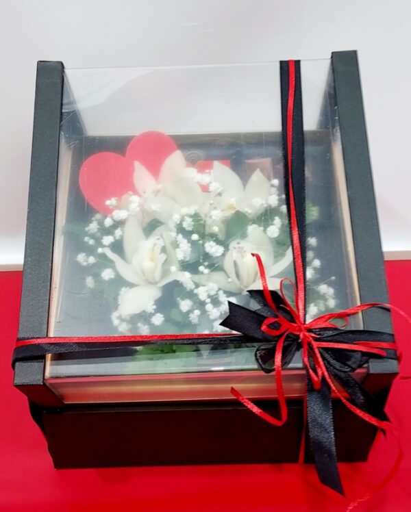 Πολυτελές  κραφτ κουτί με σκέπασμα πλέξιγλας  διάσταση 24χ24.Λουλούδια ορχιδέες συμπίντιουμ,και μαύρη σοκολάτα με γεύση πορτοκάλι